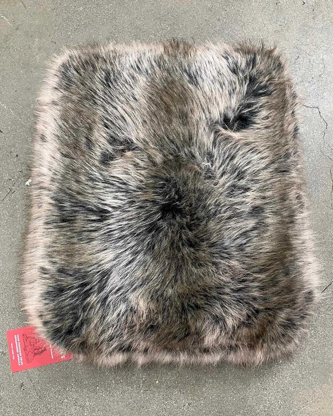 Faux fur square pillow on a concrete surface with a visible brand tag.