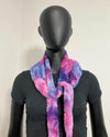 A fuzzy tie-dye scarf in pink, purple, and blue, styled on a black mannequin torso against a plain off-white background.