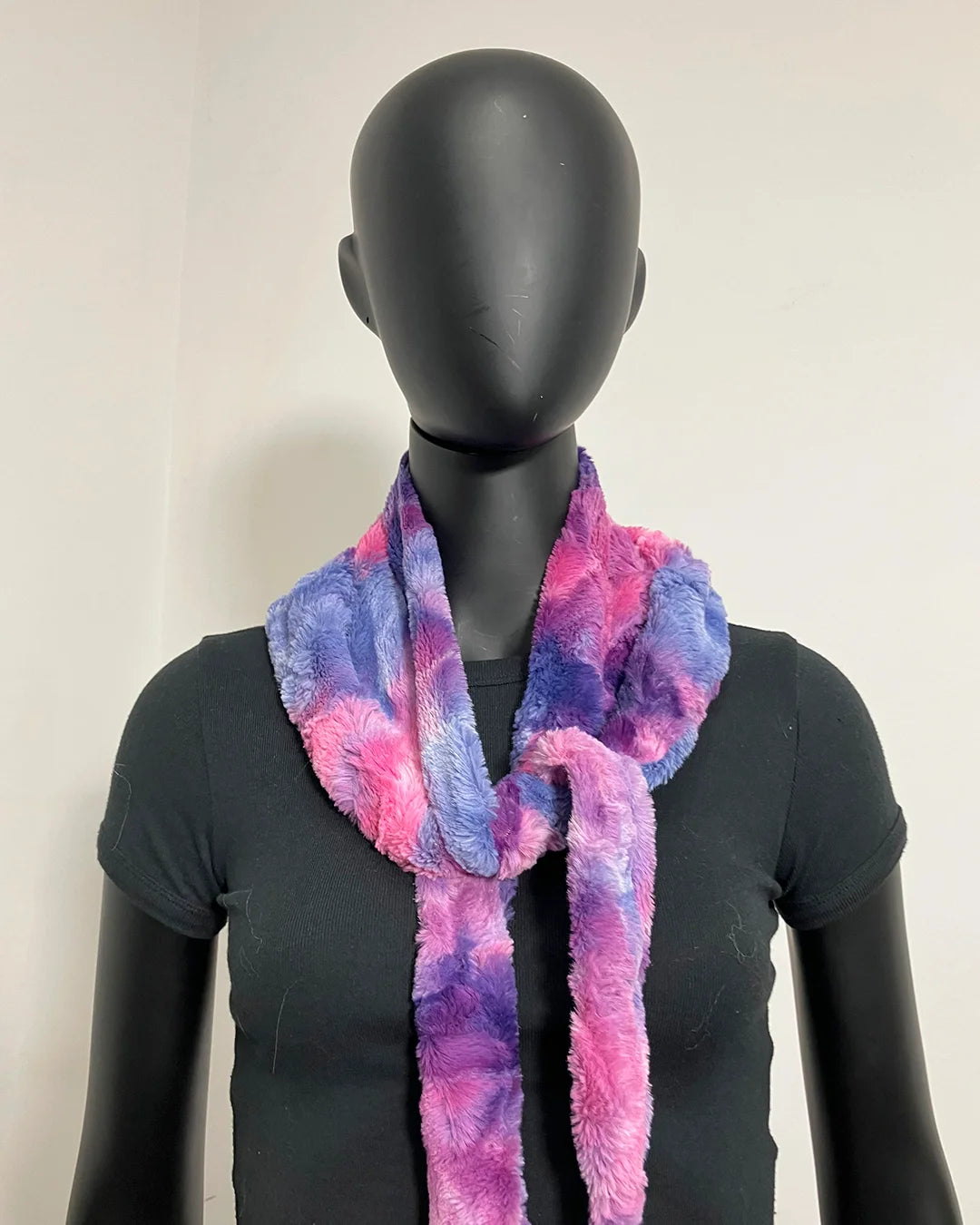 A fuzzy tie-dye scarf in pink, purple, and blue, styled on a black mannequin torso against a plain off-white background.
