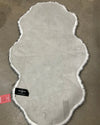 Gray faux suede backing on the fake fur husky rug with white fringe on a concrete floor, featuring a SpiritHoods label.