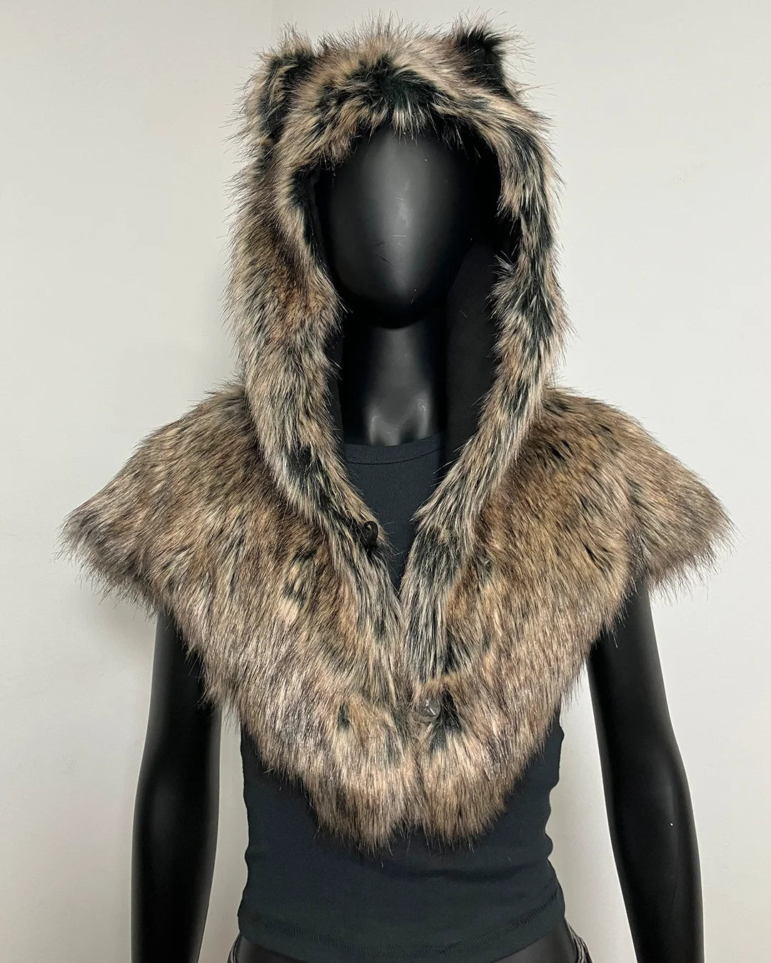 A faux fur hooded vest with animal ears on the hood and a wide collar, displayed on a black mannequin torso against a plain light gray background.