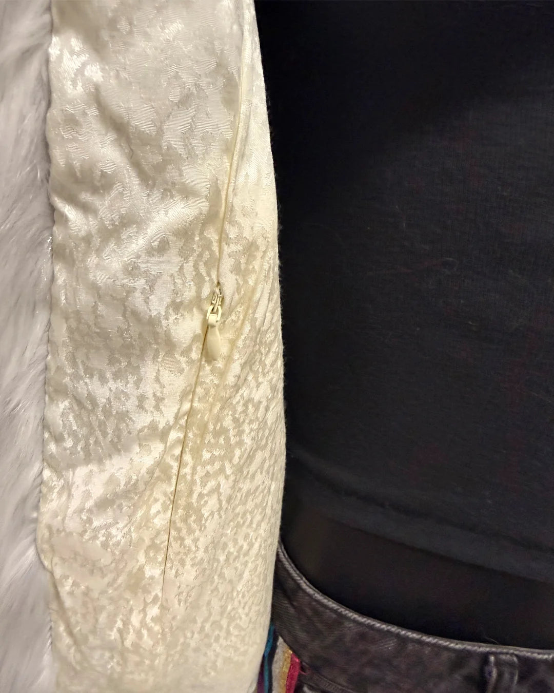 Close-up of a textured ivory snake skin lining fabric with a inner zipper pocket on a dark background