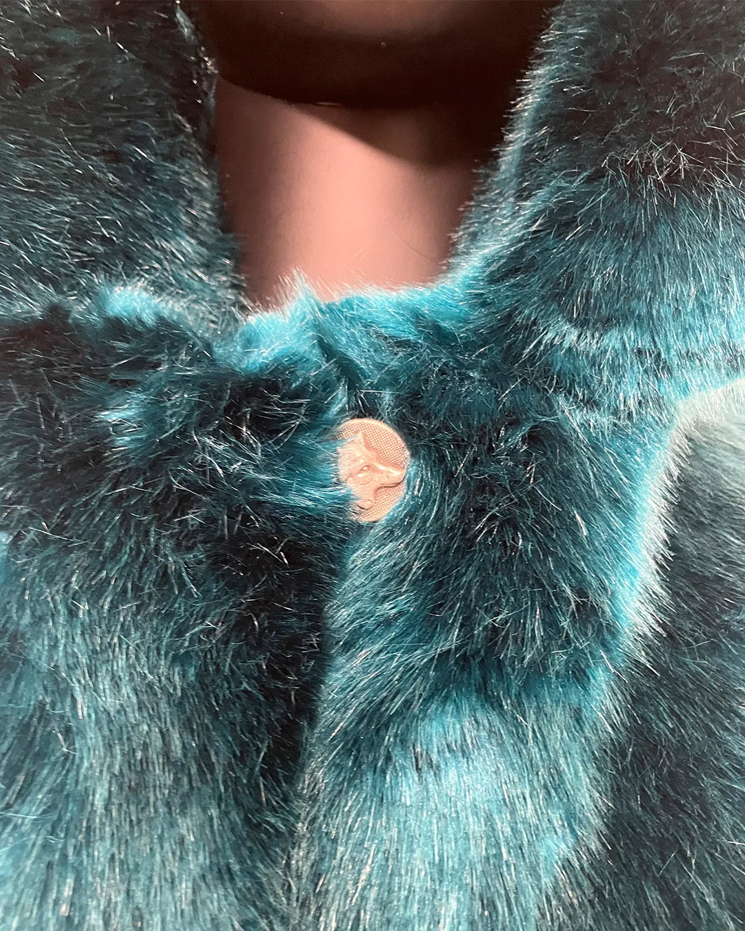 Close-up of teal faux fur fabric with a wolf face button. Showing close up of the peacoat button closure