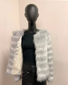 Mannequin wearing a black outfit with a silver and white fake fur jacket on a beige background