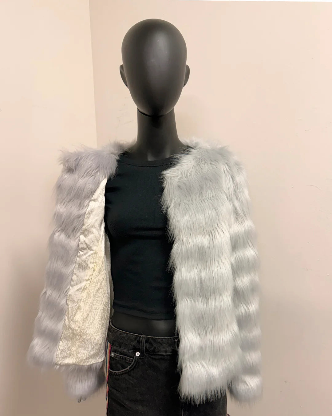 Mannequin wearing a black outfit with a silver and white fake fur jacket on a beige background