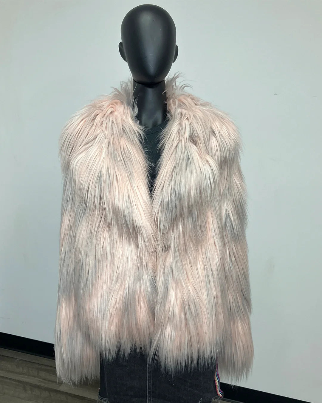 A shaggy faux fur coat in a pale pinkish-beige and grey color, displayed on a black mannequin torso against a plain light gray wall.
