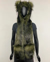 A long, shaggy faux-fur hooded scarf or vest in olive green and black, displayed on a black mannequin against a plain off-white wall.