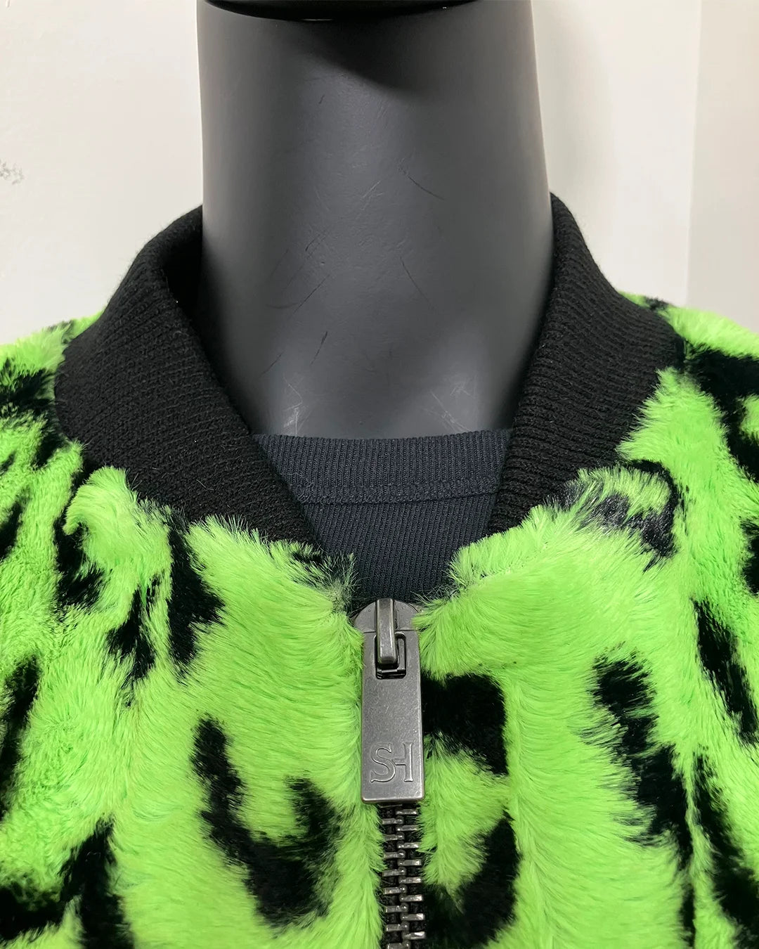 Mannequin wearing a green and black patterned jacket with a zipper. 