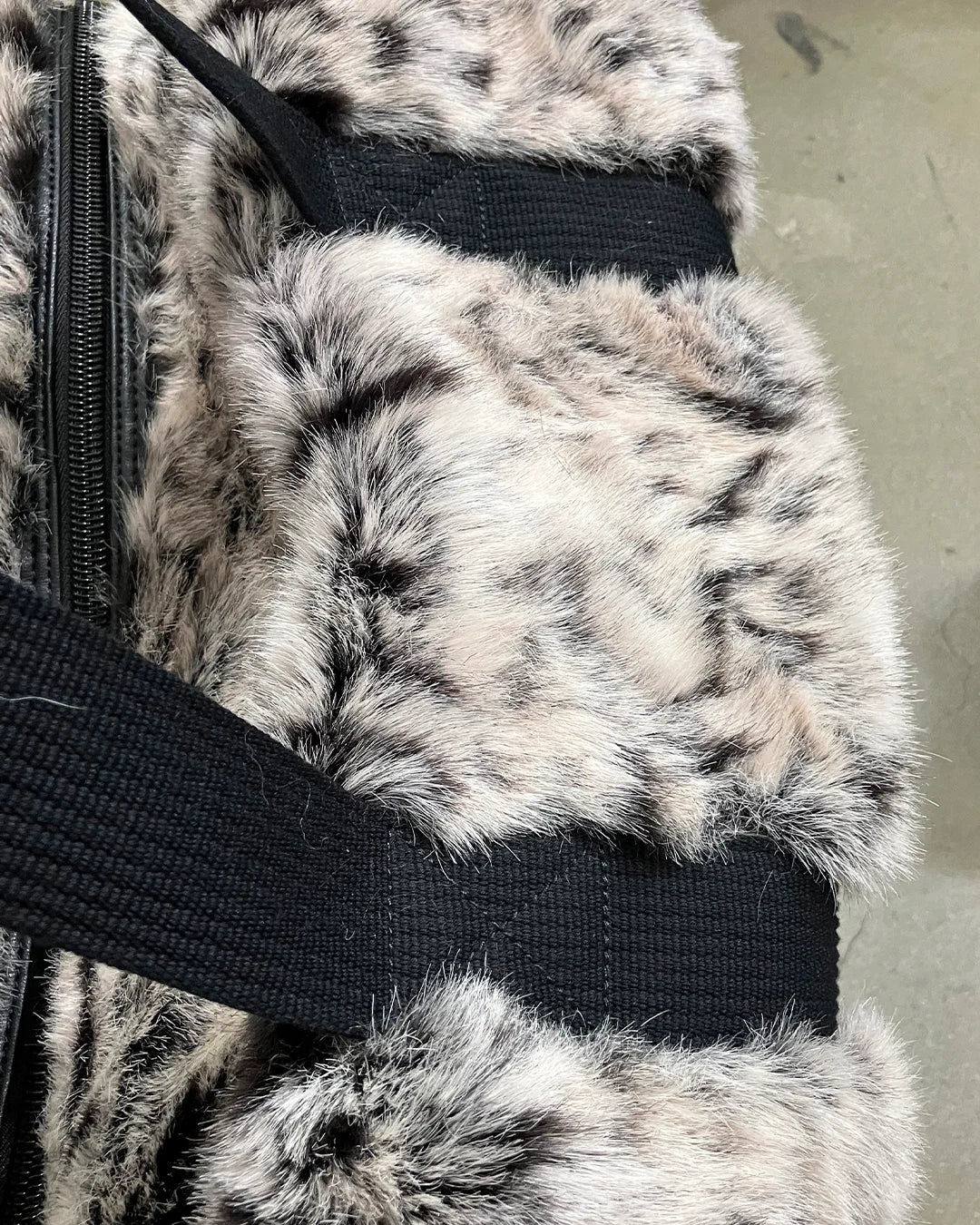 Close-up of a fake fur weekender duffle bag with a black strap on a neutral background