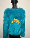 Turquoise fluffy faux fur jacket with a rainbow and star design on a mannequin against a beige background