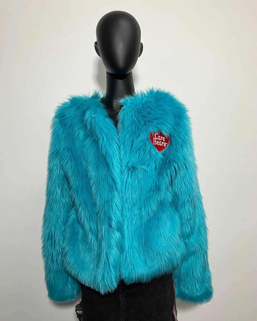 Turquoise faux fur jacket with a red Care Bears heart patch on a mannequin against a plain background