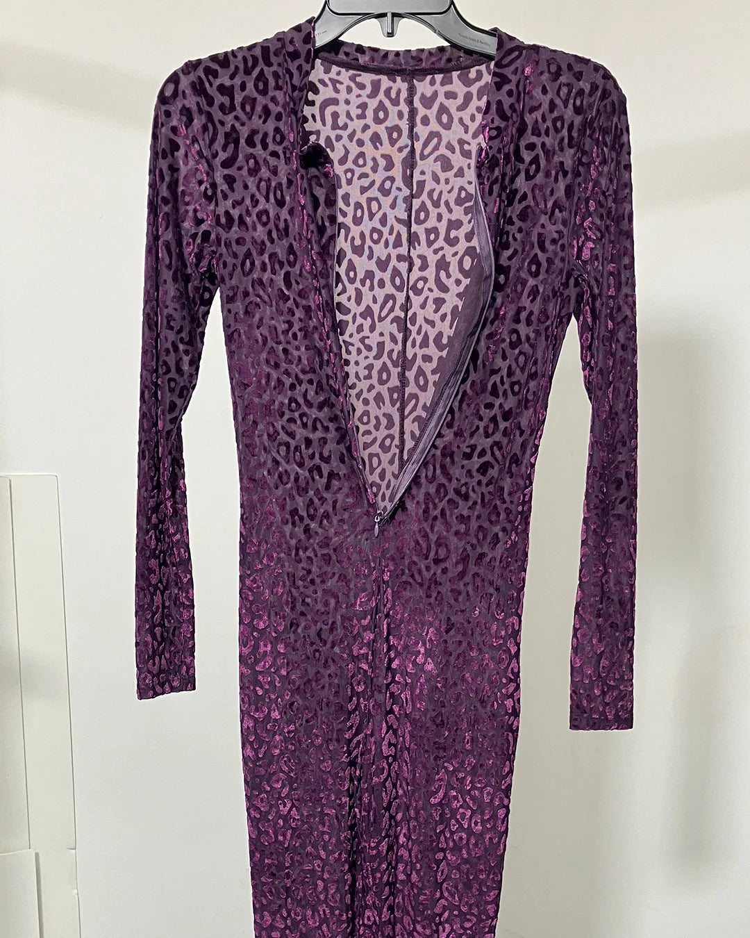 A long-sleeve purple leopard-print dress hanging on a black hanger against a plain white wall.