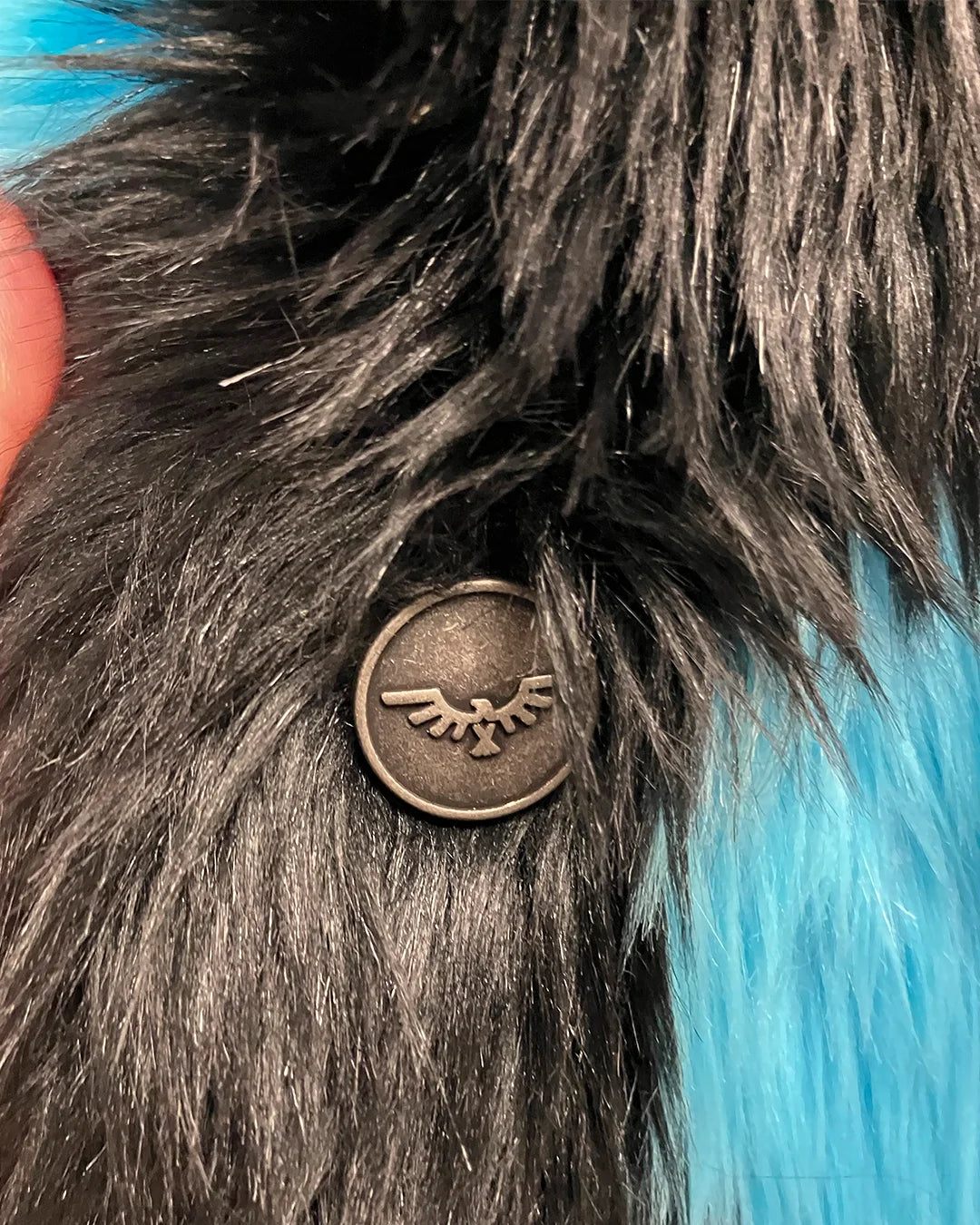 Close-up of a faux fur coat with a metallic emblem featuring wings.