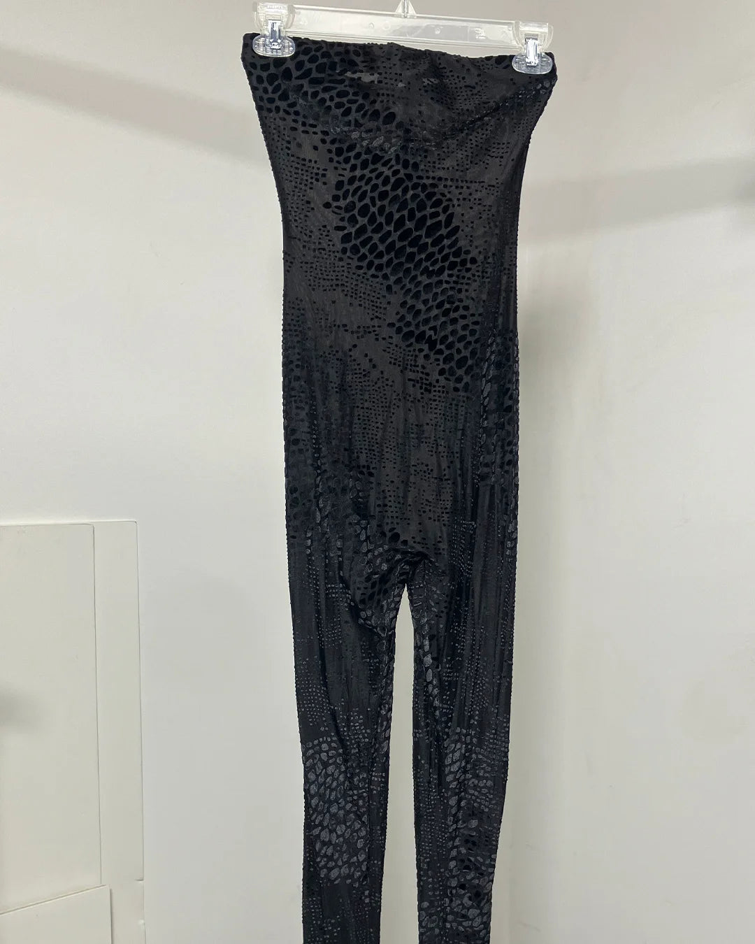 Black snakeskin-patterned strapless bodysuit hanging from a clear plastic hanger against a plain white wall.