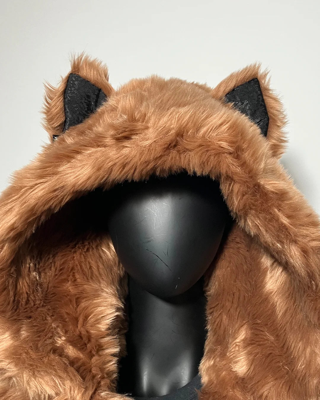 Brown furry hood with wolf ear accents on a mannequin head against a white background
