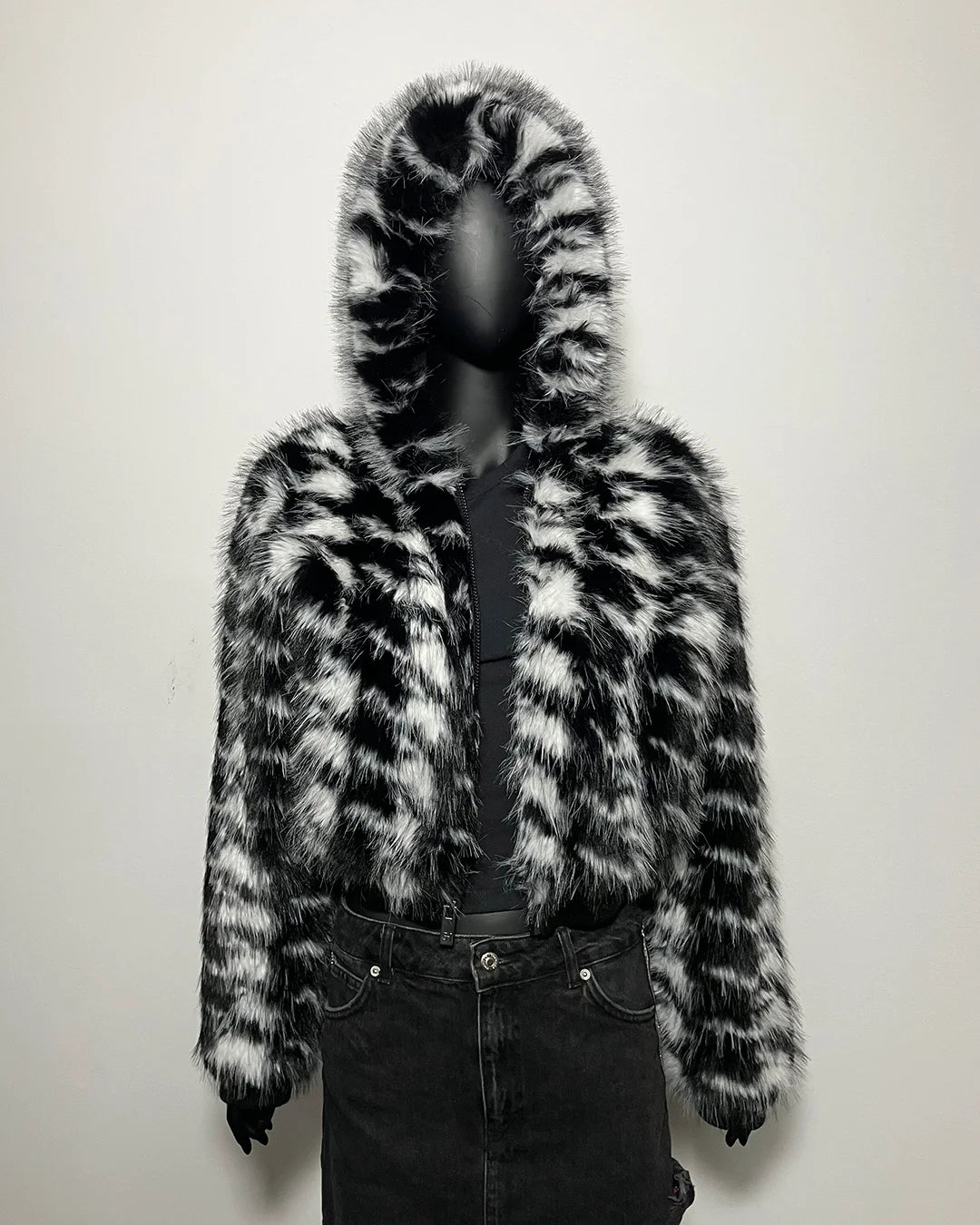 Mannequin wearing a black and white fur coat with a hood against a plain background
