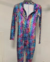 A long-sleeve, one-piece full-zip costume jumpsuit with a vibrant, multicolored abstract pattern in shades of blue, pink, purple, and yellow, displayed on a hanger against a plain light gray wall.