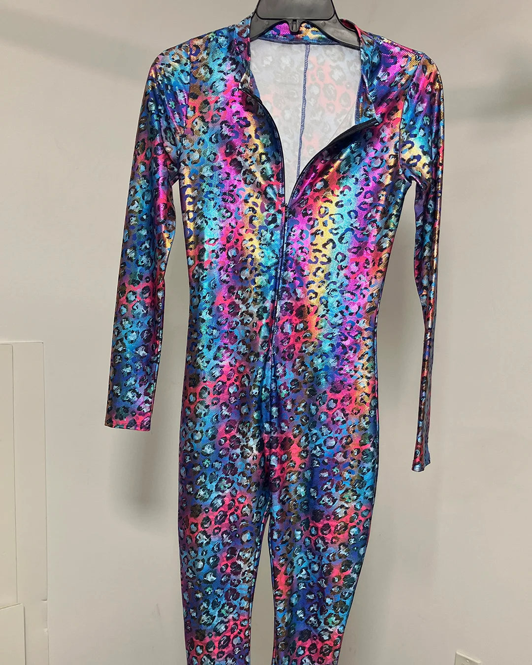 A long-sleeve, one-piece full-zip costume jumpsuit with a vibrant, multicolored abstract pattern in shades of blue, pink, purple, and yellow, displayed on a hanger against a plain light gray wall.