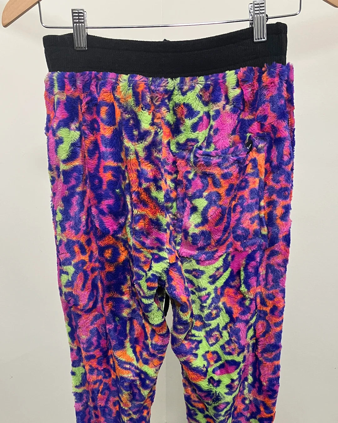 Colorful neon leopard print pants on a hanger against a white background