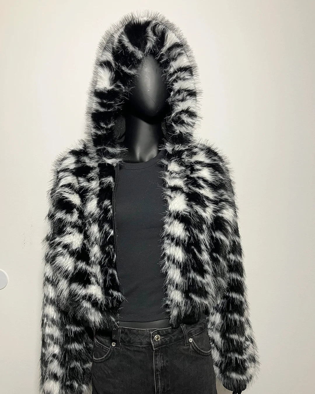 Mannequin wearing a black and white fake fur coat on a plain background