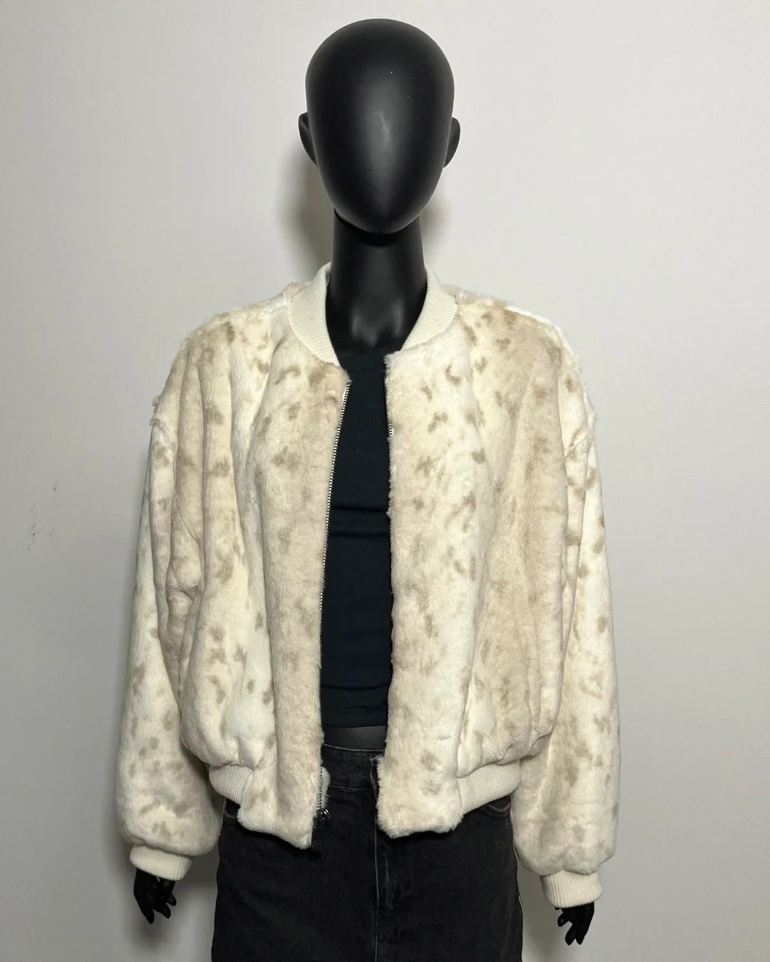 Mannequin wearing a white fake fur snow leopard-patterned jacket over a black outfit on a plain background
