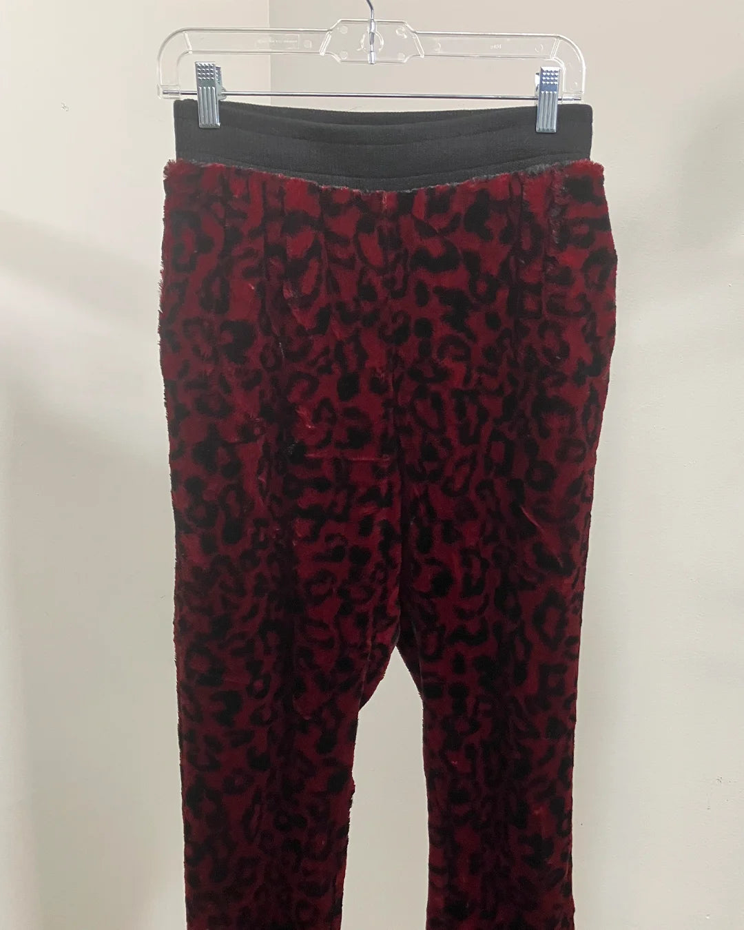 Red and black leopard print pants on a hanger against a beige background