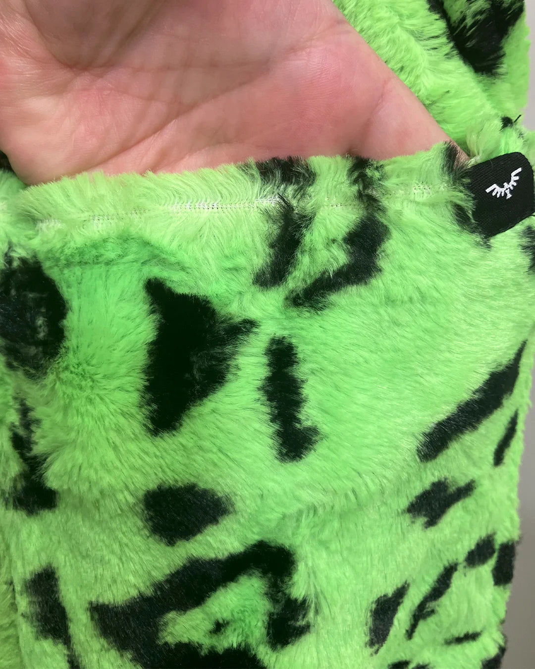 Close-up of green fabric with black patterns held by a hand, with a brand tag visible.