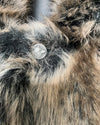 Close-up of a fluffy grey, brown and black faux fur coat with a button featuring a wolf design.