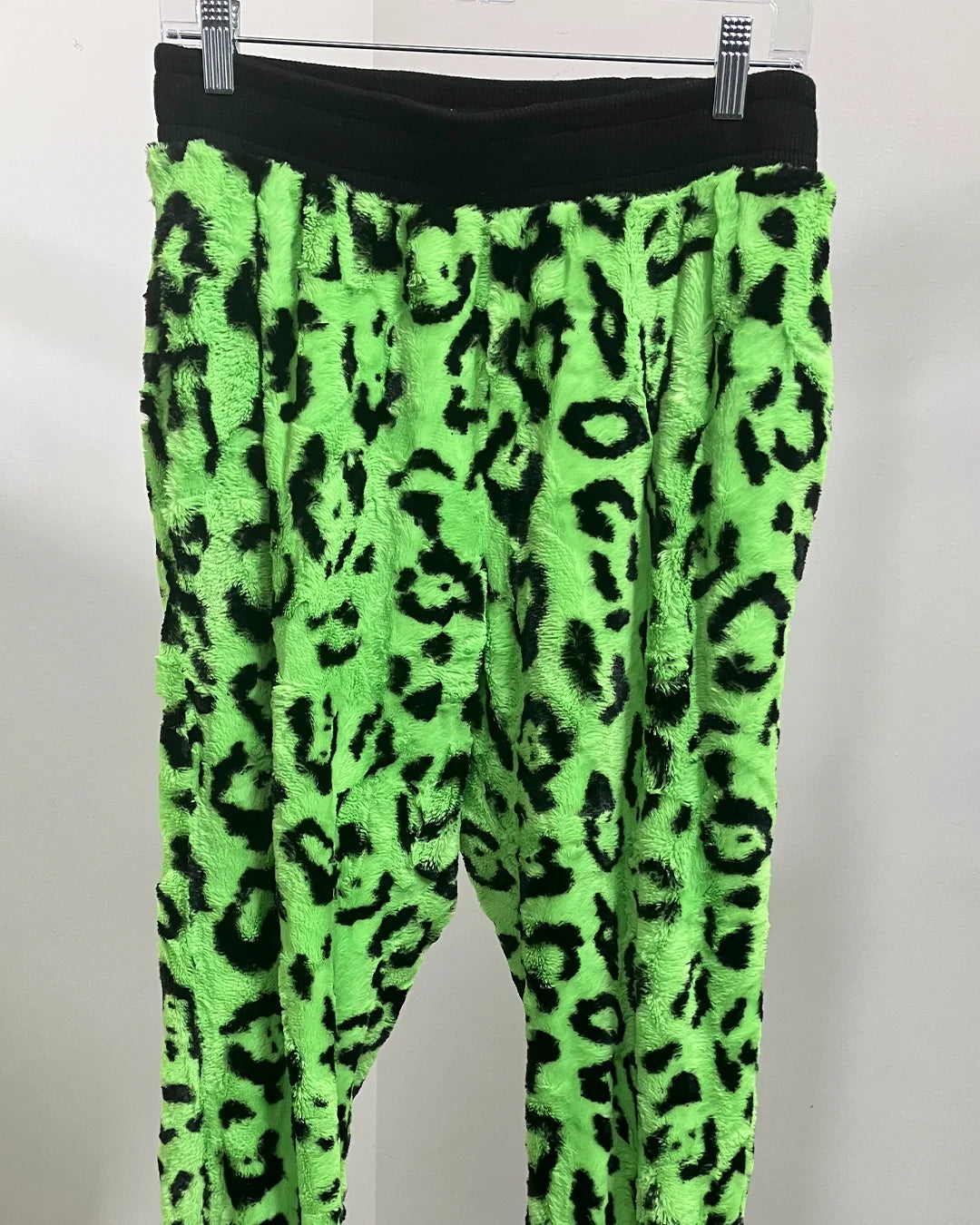 Neon green leopard print pants on a hanger against a white background