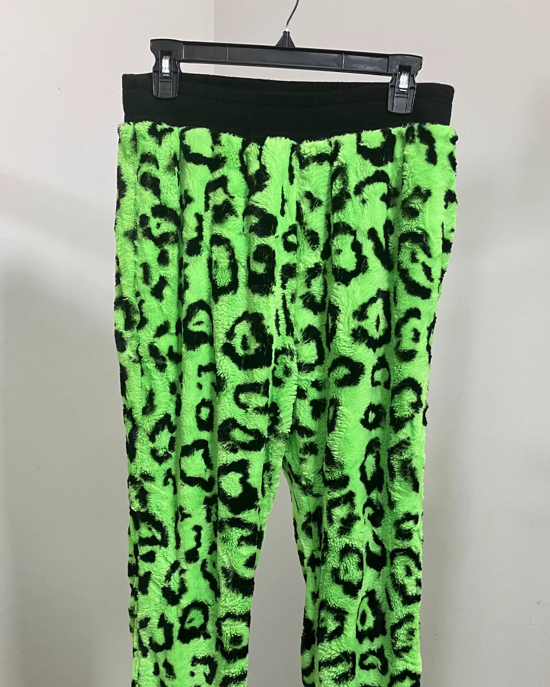 Neon green pants with black leopard print pattern on a hanger against a white background