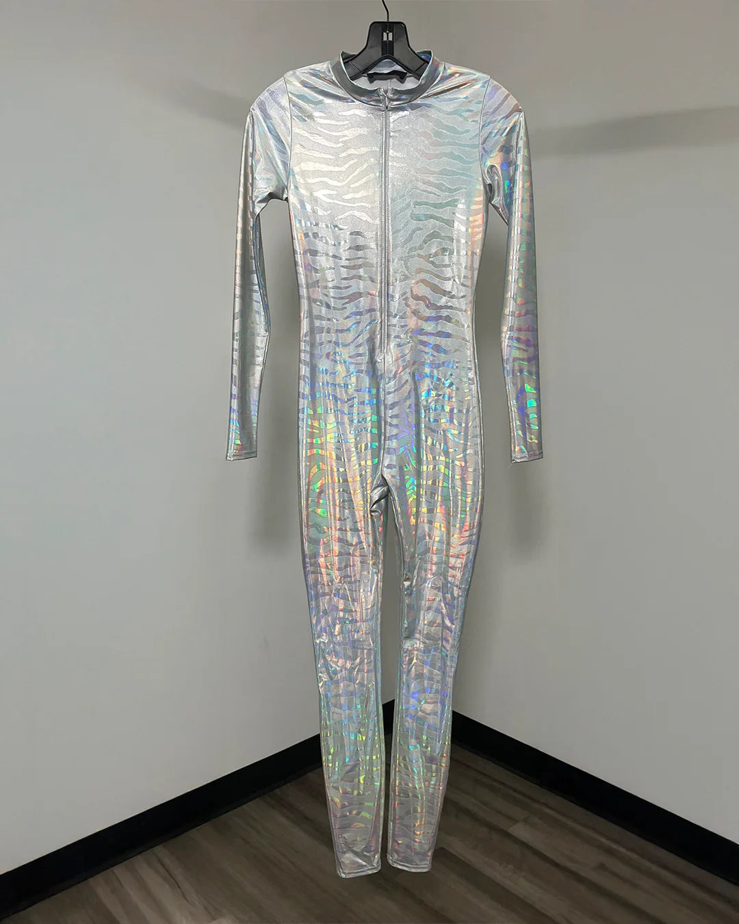 A full-body silver holographic jumpsuit with a front zipper and hood, hanging on a black hanger against a plain gray wall.