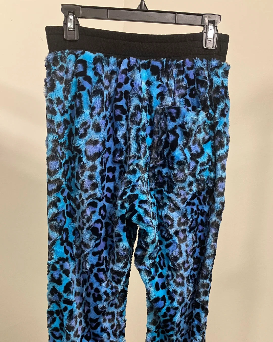 Blue leopard print sweatpants on a hanger against a beige background