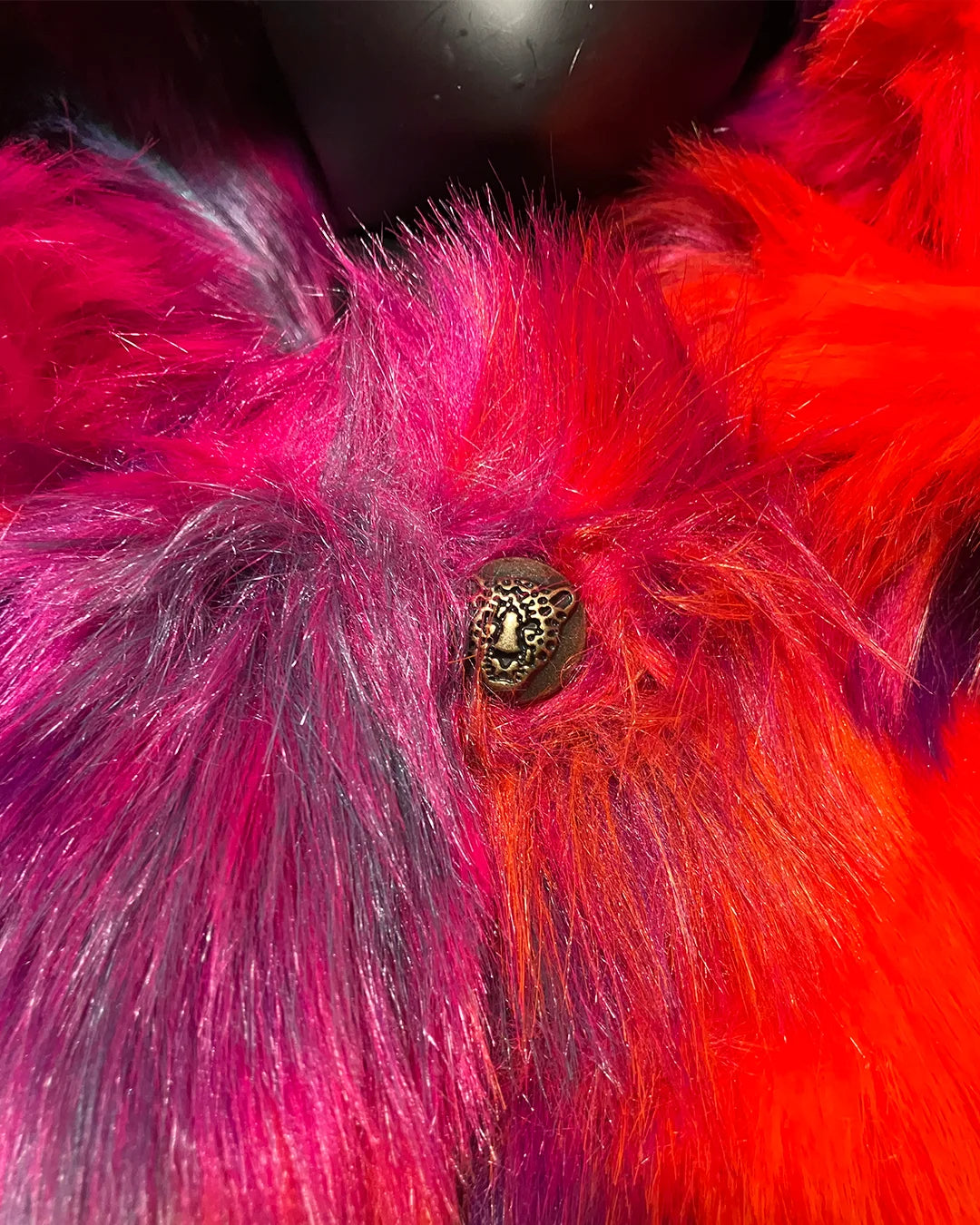 Close-up of a fluffy pink and red faux fur coat with a decorative leopard face button in the center.
