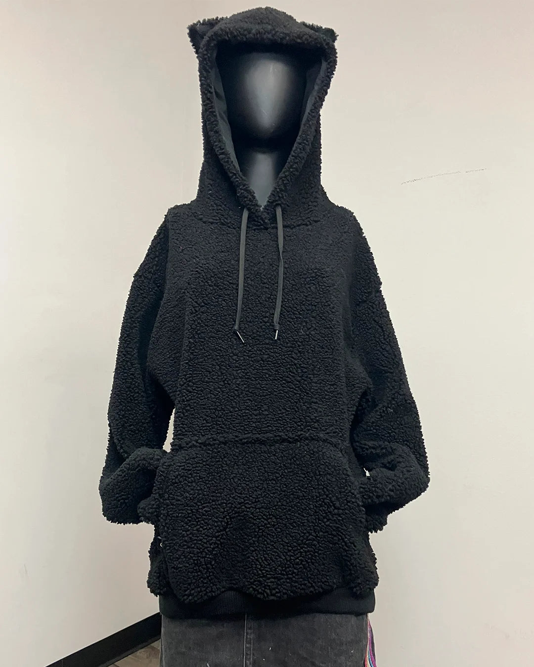 A black sherpa fleece hoodie with a plush teddy texture, displayed on a black mannequin torso. The hoodie features a large hood with cat-like ears, dark gray drawstrings, and a front kangaroo pocket.