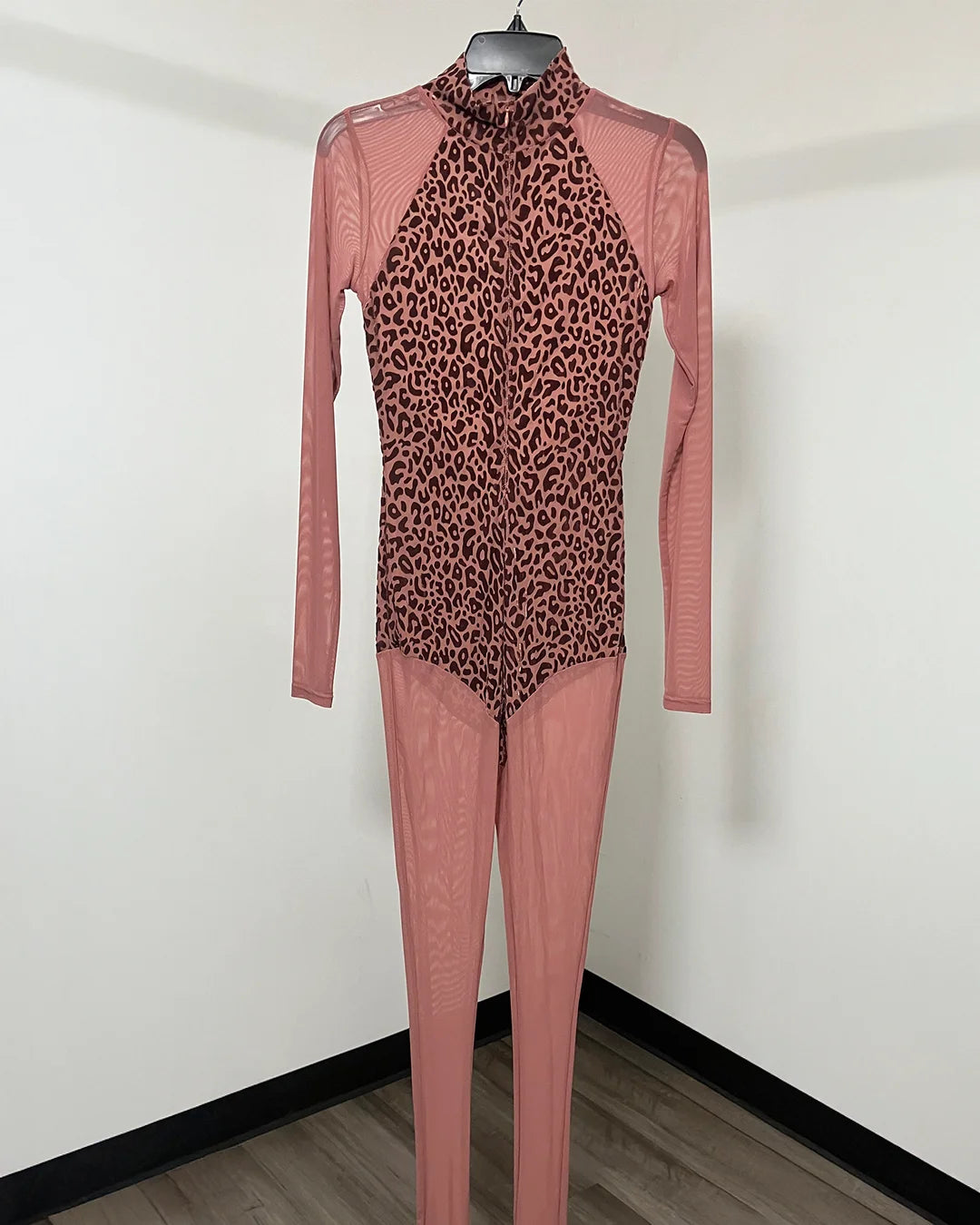 A long-sleeve bodysuit with a leopard print front panel and solid dusty pink sleeves, collar, and leg sections, displayed on a hanger against a plain white wall.