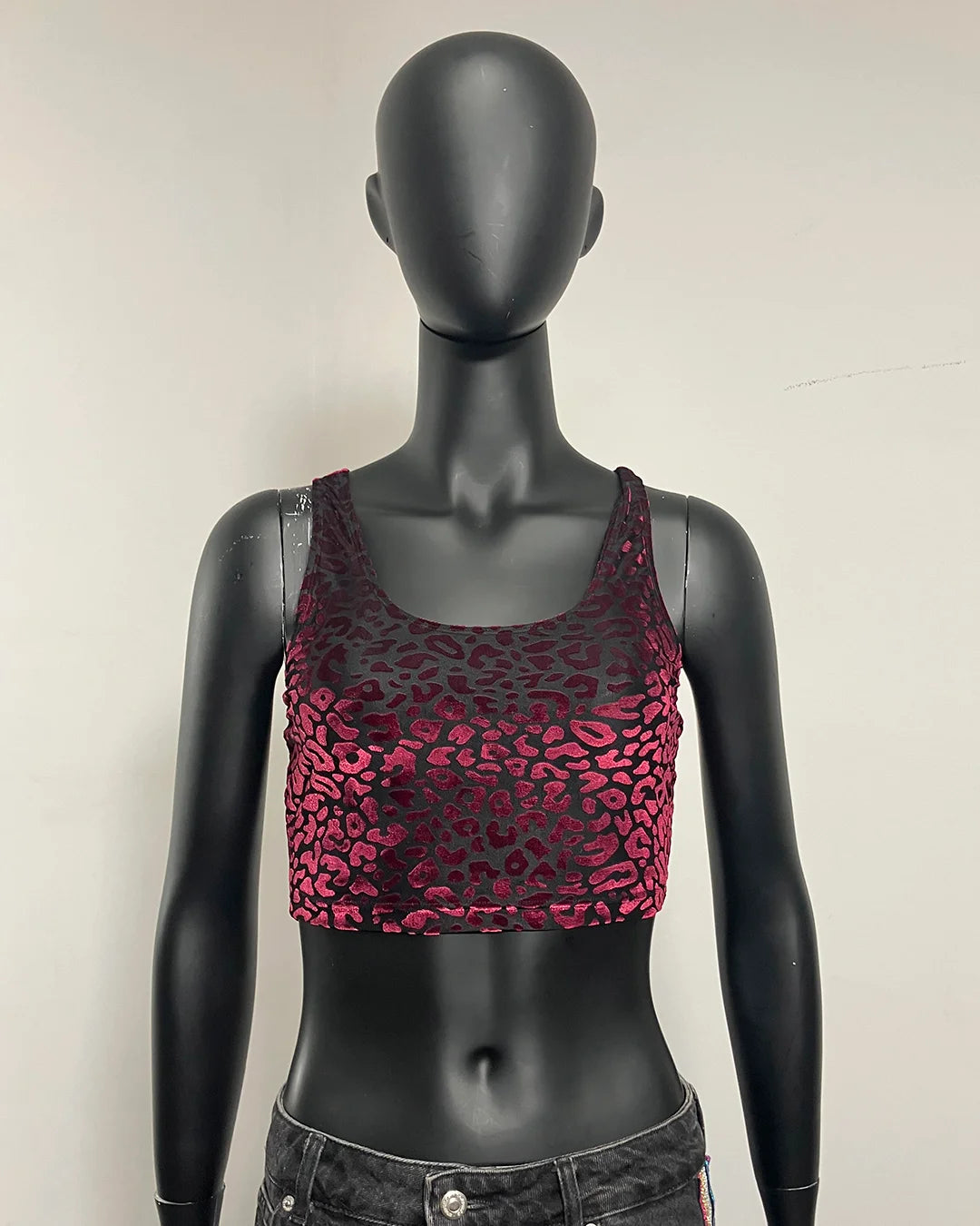 A sleeveless crop top with a metallic magenta and black leopard print pattern, displayed on a black mannequin torso.