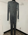 A long-sleeve, full-length jumpsuit covered in shimmering silver sequins, displayed on a black hanger against a plain white wall.