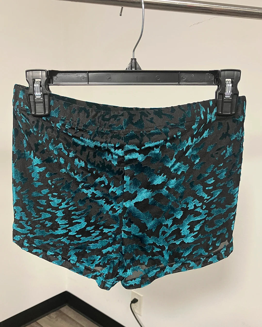 A pair of women's shorts with a black and teal abstract tiger print pattern, hanging on a black hanger.