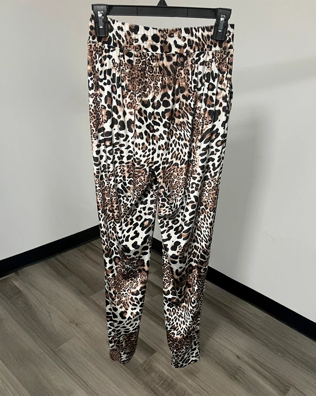 Leopard print ankle-length leggings hanging on a black hanger against a plain wall and wood-look floor.