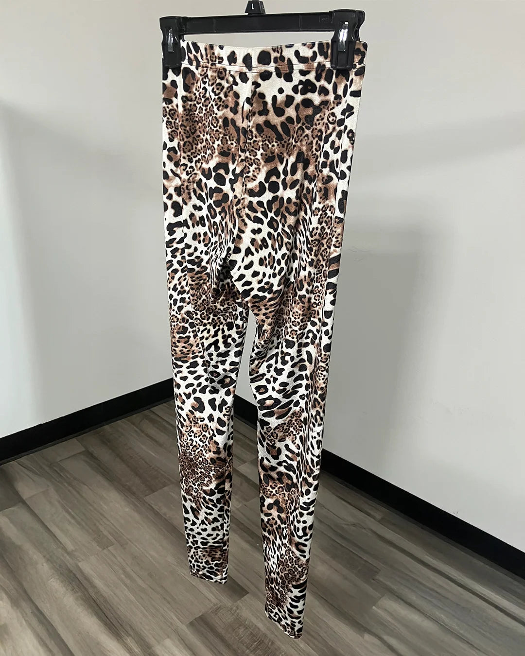 Leopard print leggings hanging on a black hanger against a white wall and wood-look floor.