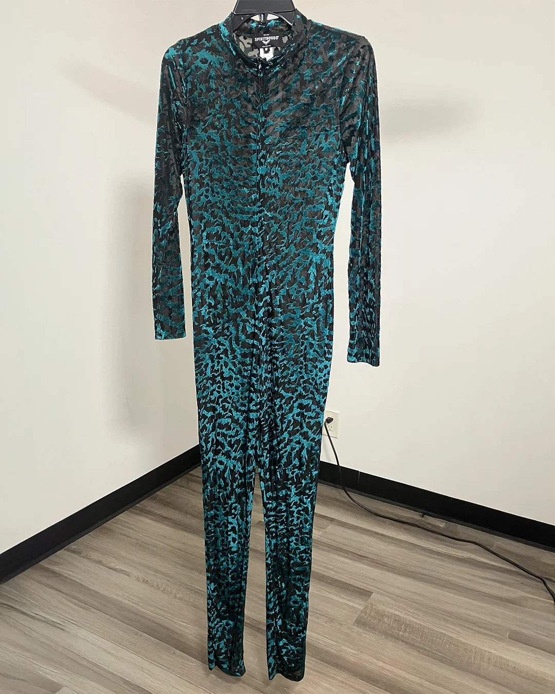 A long-sleeve, full-length jumpsuit with a mock neck, featuring an abstract black and teal tiger print pattern, displayed on a hanger against a plain wall.