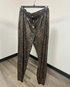 Leopard print jogger pants hanging on a black hanger against a plain off-white wall with a wood-look floor.