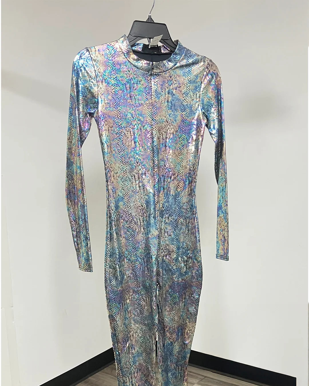 A long-sleeve, full-length one-piece jumpsuit with a high mock neck, covered in a shimmering iridescent holographic pattern of blue, purple, pink, and silver, displayed on a hanger against a plain white wall.