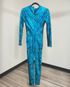 A long-sleeve one-piece jumpsuit in a vibrant blue and black abstract animal print pattern, hanging on a black hanger against a plain wall with wood flooring.
