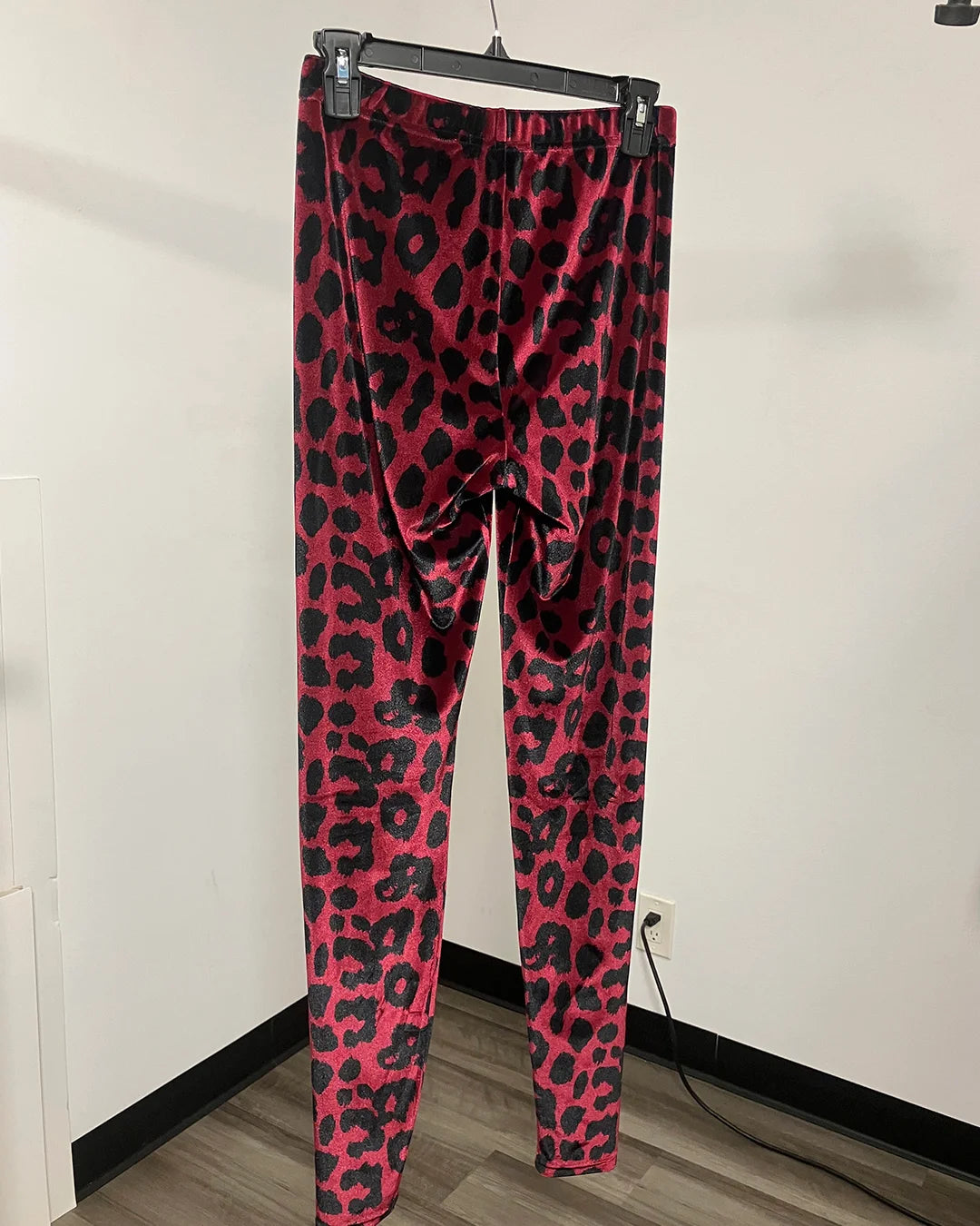Pink and black leopard print leggings hanging on a black hanger against an off-white wall.