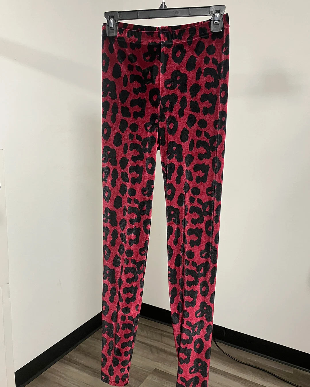 Pink and black leopard print leggings hanging on a black hanger against a plain white wall.