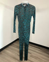 A long-sleeve, full-length one-piece jumpsuit with an abstract teal and black animal-like pattern, hanging on a clear plastic hanger against a plain white wall with a wood-look floor.