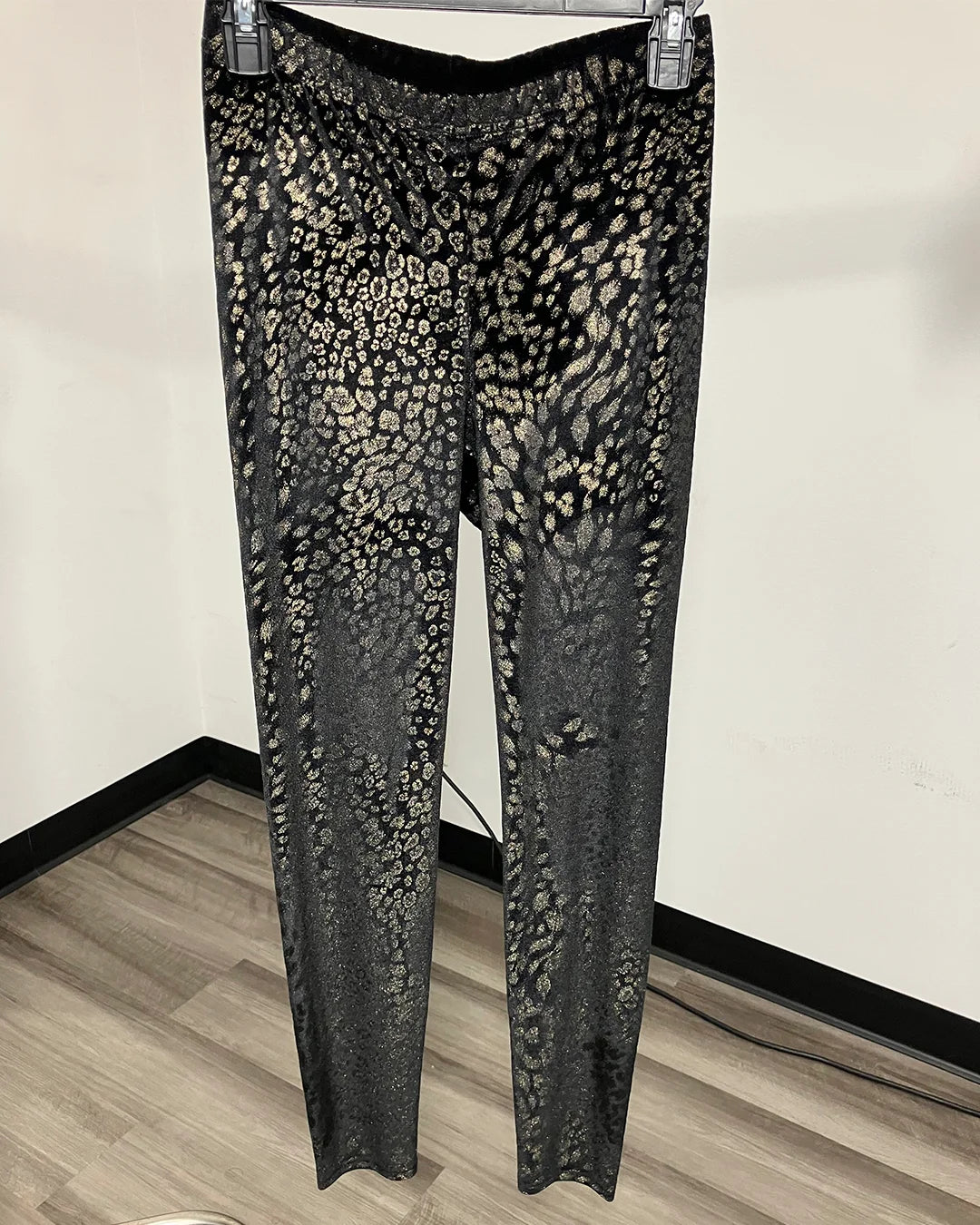 Black and beige leopard-print velvet pants hanging on a hanger against a plain indoor wall.