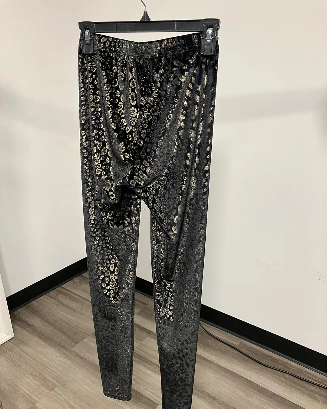 Black and gray snakeskin print leggings hanging on a black hanger against a white wall and wood floor.
