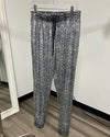 Gray and black metallic snakeskin print joggers hanging on a clear plastic hanger against a white wall.